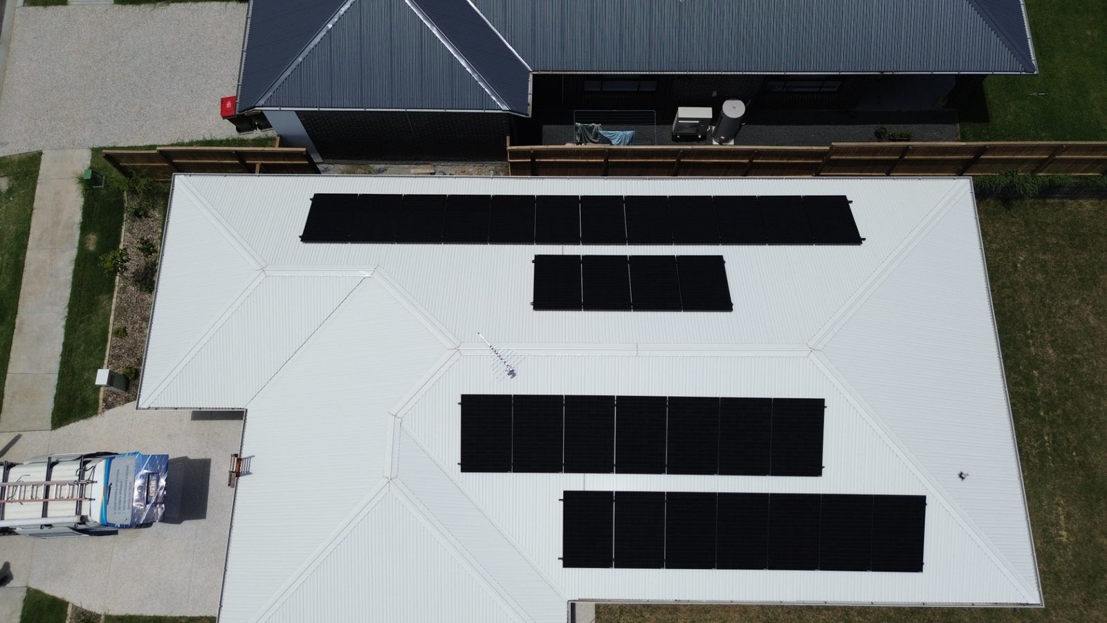 Aerial drone view of a large residential solar installation — all-black panels on a Colorbond roof with the Focus Solar & Electrical van in the driveway